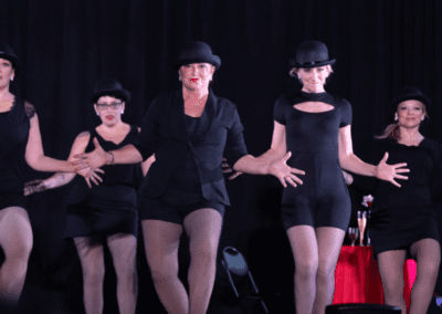 A group of women in black outfits and hats performing on stage.