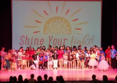 A diverse group of children and adults performing on stage at a school event.